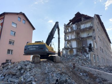 Arnoldstein, Avusturya - 20 Temmuz 2025: Kazıcı, bir kentsel inşaat alanındaki enkaz ve molozlarla çevrili bir binayı aktif olarak yıkıyor