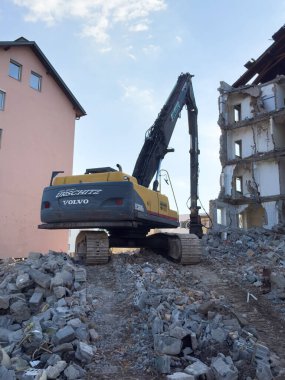 Arnoldstein, Avusturya - 20 Temmuz 2025: Volvo kazıcısı, bir inşaat alanındaki enkaz ve molozlarla çevrili bir yapıyı aktif olarak yıkıyor