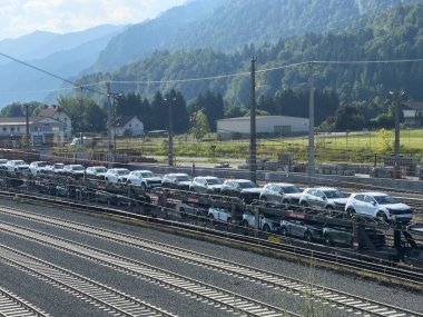 Arnoldstein, Avusturya - 20 Temmuz 2025: Araçlar, dağlarla ve yeşilliklerle döşenmiş demiryolu yük vagonlarına yüklendi