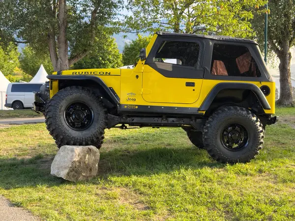 Villach, Avusturya - 20 Temmuz 2025: Sarı Jeep Rubicon çimenli bir arazide bir kayanın üzerinde konumlandırılmış, güçlü özelliklerini ve maceracı ruhunu vurguluyor