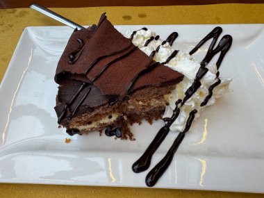 Çürümüş çikolatalı kek dilimi, çırpılmış krema ve beyaz tabakta çikolata serpiştirilmiş..