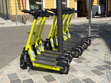 Villach, Avusturya - 24 Temmuz 2025: Sarı elektrikli scooterlar kaldırıma düzgün park edilmiş, kentsel ulaşım seçenekleri ve şehir sakinleri için kolaylıklar vurgulanıyor