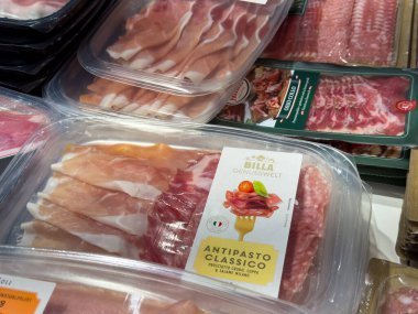 Villach, Avusturya - 24 Temmuz 2025: Pişirilmiş et ve peynirlerle paketlenmiş antipasto çeşidi, mutfak tutkunları için bakkalda güzelce düzenlenmiştir