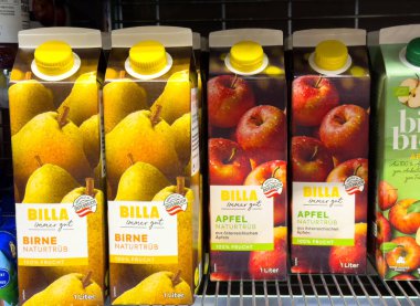 Villach, Avusturya - 24 Temmuz 2025: Süpermarket raflarında armut ve elma aromalı BILLA meyve suyu kutuları, renkli ambalajlar ve taze meyve betimlemeleri