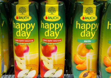 Villach, Avusturya - 24 Temmuz 2025: Rauch Happy Day meyve suyu kutuları süpermarket raflarında renkli ambalajları ve ferahlatıcı içecekleri vurgulayan bulutlu elma ve kayısı aromaları sergiliyor