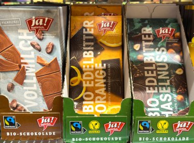 Villach, Avusturya - 24 Temmuz 2025: Organik çikolata dükkanda süt, portakal ve fındık gibi ekolojik ambalajlı ve canlı renklerde tatlar sergileniyor