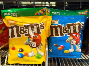Villach, Avusturya - 24 Temmuz 2025: Fıstık ve çıtır çıtır aromalı parlak renkli M & M çantaları perakende satış rafında sergilenerek şeker meraklılarını tatlı ikram etmeye davet etti