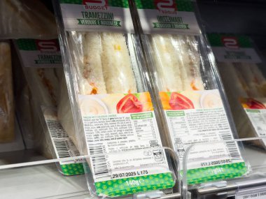 Tarvisio, İtalya - 26 Temmuz 2025: Bütçe Tramezzini sandviç paketleri bir süpermarket buzdolabında, taze malzemeler ve renkli ambalajlar eşliğinde düzgünce düzenlenmiştir