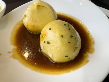 Zengin soslu ve beyaz tabakta soğanlı iki Alman patatesi köftesi..