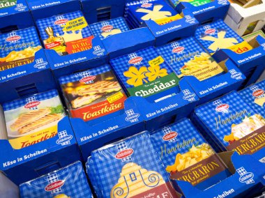 Villach, Avusturya - 28 Temmuz 2025: Değişik aroma ve markalardan oluşan, gıda tasarımı ve aşçılık projeleri için mükemmel mavi kutularda canlı peynir dilimleri gösterimi