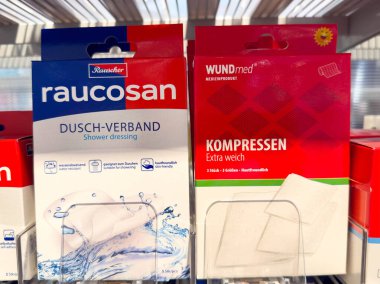 Villach, Avusturya - 28 Temmuz 2025: Raucosan duş elbisesi ve Wundmed kompresi bir rafta sergilenerek, yara bakımı için gerekli tıbbi malzemelerin altı çizildi