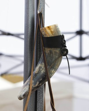 Deri kayışlarla metal yapıdan sarkan boynuz içme kabı..