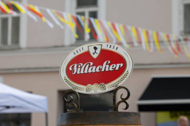 Villach, Avusturya - 28 Temmuz 2025: Renkli dekorasyonlar ve hareketli bir atmosferle çevrili bir açık hava pazarında kötü adam birası