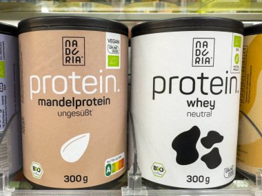 Villach, Avusturya - 30 Temmuz 2025: Protein tozu kapları süpermarket raflarında badem ve beyaz protein seçenekleri sergiliyor, besin ve sağlık faydalarını vurguluyor