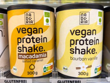 Villach, Avusturya - 30 Temmuz 2025: Vejetaryen protein karışımı kaplar Macadamia tuzlu karamel ve burbon vanilyalı tatları bir market rafında sergiliyor