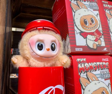 Villach, Avusturya - 30 Temmuz 2025: Kırmızı şapkalı sevimli plastik karakter renkli ambalajlarla çevrili bir bardaktan bakıyor ve eğlenceli bir atmosfer yaratıyor