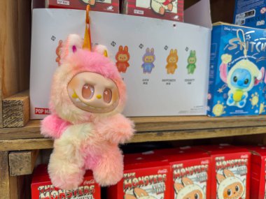 Villach, Avusturya - 30 Temmuz 2025: Sevimli peluş tek boynuzlu at oyuncağı çeşitli renkli ürünlerle dolu bir rafta sergileniyor, neşeli bir atmosfer yaratıyor.