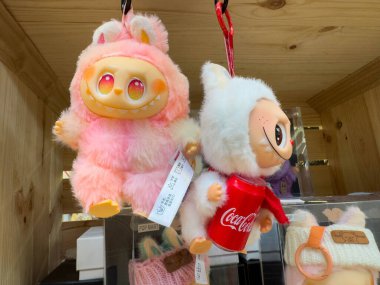 Villach, Avusturya - 30 Temmuz 2025: Renkli pelüş oyuncaklar sergilendi, biri büyük gözlü pembe, diğeri Coca-Cola kıyafetli, neşeli özünü ve canlı tasarımını yakalayan beyaz