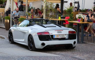 Velden, Avusturya - 18 Haziran 2025: Audi R8 Spyder açık hava yemekleri, lüks ve canlı şehir hayatı ile hareketli bir caddeye park etti