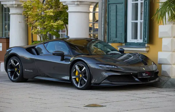 Velden, Avusturya - 18 Haziran 2025: Ferrari SF90 Stradale tarihi bir binanın yakınına park edilmiş, parlak hatlarını ve lüks tasarımını canlı bir şekilde vurguluyor.