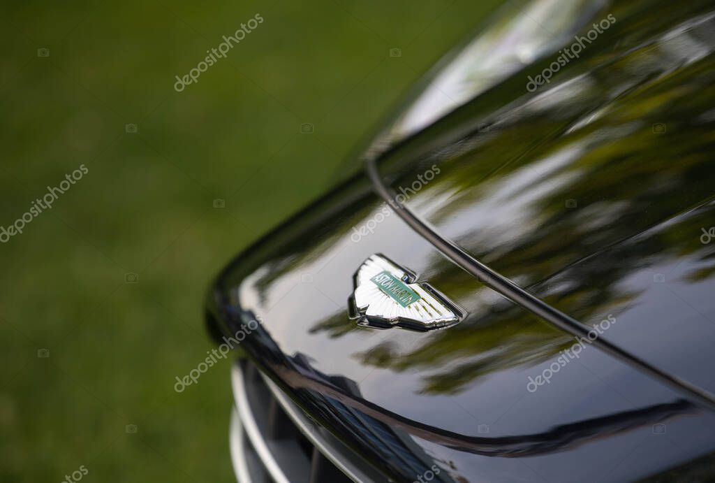 Velden, Austria - June 18, 2025: Aston Martin emblem shines on glossy black sports car hood, surrounded by lush green grass, highlighting elegance and sophistication