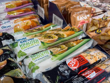 Villach, Avusturya - 15 Ağustos 2025: Renkli abur cuburlar ve gıda ürünleriyle çevrili bir market koridorunda paketlenmiş sebze baget satılıyor