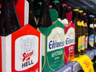 Villach, Avusturya - 15 Ağustos 2025: Stiegl Hell ve Edelweizen Hefeweizen bira şişeleri benzersiz tasarımları ve renkleri ön plana çıkarılarak bir süpermarket rafına yerleştirilmiştir.