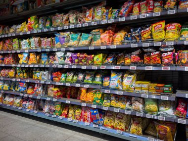 Villach, Avusturya - 15 Ağustos 2025: Market abur cubur reyonu kolay seçim için düzgün düzenlenmiş paketlerde renkli cips ve atıştırmalıklar sergiliyor