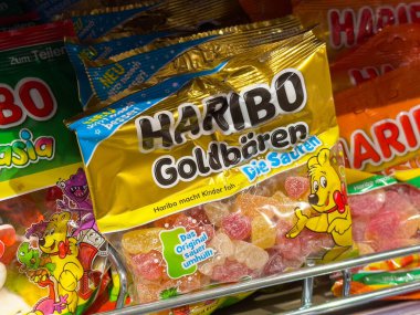 Villach, Avusturya - 15 Ağustos 2025: Haribo Goldbaren jelibon ayıcıkları çeşitli şekerlemelerle dolu bir mağaza rafında renkli ambalajlarla öne çıkmıştır