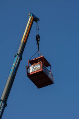 Faak Am See, Avusturya - 09 Ağustos 2025: Crane gökyüzünde kırmızı bir platform kaldırıyor, kullanılan endüstriyel çevre ve makineleri vurguluyor