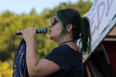 Faak Am See, Avusturya - 09 Ağustos 2025: Canlı açık hava festivalinde yeşil saçlı kadın vokalist mikrofona şarkı söyleyerek enerjik bir ortam yarattı