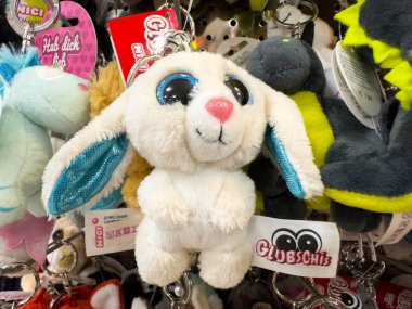 Villach, Avusturya - 18 Ağustos 2025: Büyük mavi gözlü ve pembe burunlu şirin beyaz tavşancık anahtarlığı, canlı bir ortamda çeşitli renkli pelüş oyuncakların arasına yerleştirilmiş