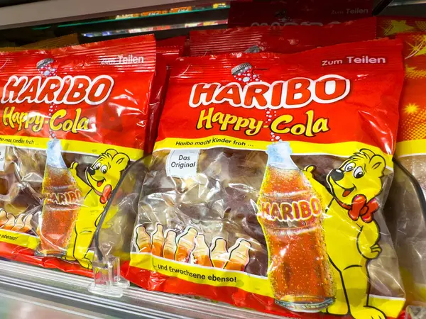Villach, Avusturya - 18 Ağustos 2025: Haribo Happy Cola şekerleri bir süpermarket rafında düzgün bir şekilde düzenlenmiştir, parlak renkler ve eğlenceli tasarımlar içerir.
