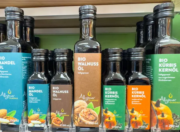 Villach, Avusturya - 18 Ağustos 2025: Rafa dizilmiş organik yağ şişeleri, renkli etiketler ve doğal malzemelerle ceviz, balkabağı ve badem yağları vurgulanıyor