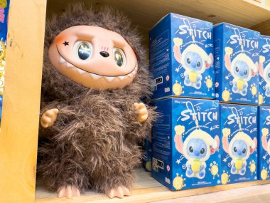 Villach, Avusturya - 21 Ağustos 2025: Tüylü pelüş oyuncak ahşap rafta, canlı bir perakende ortamında Stitch ürünlerinin yanında sergileniyor