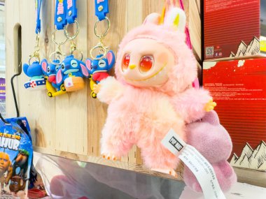 Villach, Avusturya - 21 Ağustos 2025: Canlı bir perakende piyasasında renkli anahtarlıkların yanında büyük gözlü sevimli pembe peluş oyuncak
