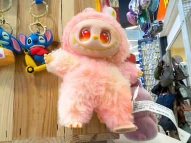 Villach, Avusturya - 21 Ağustos 2025: Canlı bir mağaza ortamında renkli anahtarlıklar arasında sergilenen büyük gözlü sevimli pembe peluş oyuncak