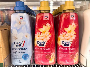 Villach, Avusturya - 21 Ağustos 2025: Denk mit kumaş yumuşatıcı şişeleri, çamaşır bakım çözümleri için bir rafta sergilenen mavi ve kırmızı çiçekli tasarımlara sahiptir.