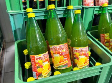 Villach, Avusturya - 21 Ağustos 2025: Apfel-Portakal suyu şişeleri bir bakkalda yeşil sandıklara yerleştirilip parlak renkleri ve tazeliği vurgulanıyor