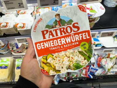 Villach, Avusturya - 21 Ağustos 2025: Hand, domates ve fesleğen içeren Patros peynir paketini canlı renklerle dolu bir market koridorunda tutuyor