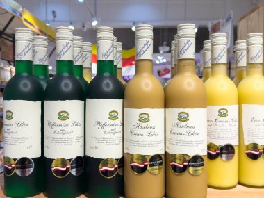 Villach, Avusturya - 21 Ağustos 2025: Çeşitli yeşil, sarı ve krem rengi likör şişeleri bir mağaza rafında düzenli olarak düzenlenmekte, müşterileri lezzetleri keşfetmeye davet etmektedir