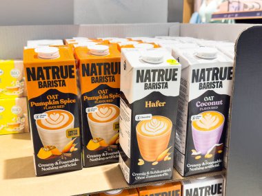 Villach, Avusturya - 21 Ağustos 2025: Kahve meraklıları için bir rafta dizilmiş balkabağı baharatı, Hindistan cevizi ve orijinal aromalı Natrue Barista yulaf sütü kutuları