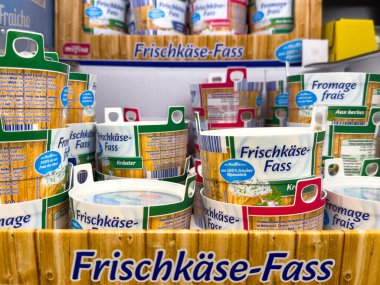 Villach, Avusturya - 21 Ağustos 2025: Frischkase-Fass peynir kapları bir marketin ahşap rafında çeşitli tatları ve çekici tasarımları vurguluyor.