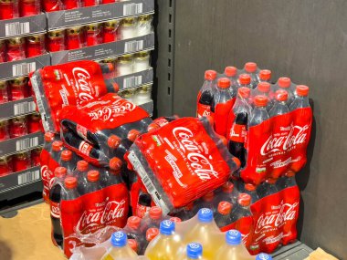 Villach, Avusturya - 21 Ağustos 2025: Parlak kırmızı ambalajlı ve çeşitli içeceklerden oluşan, pazarlama ve tanıtım amaçlı kullanım için mükemmel olan Coca-Cola şişeleri bir mağazada depolandı