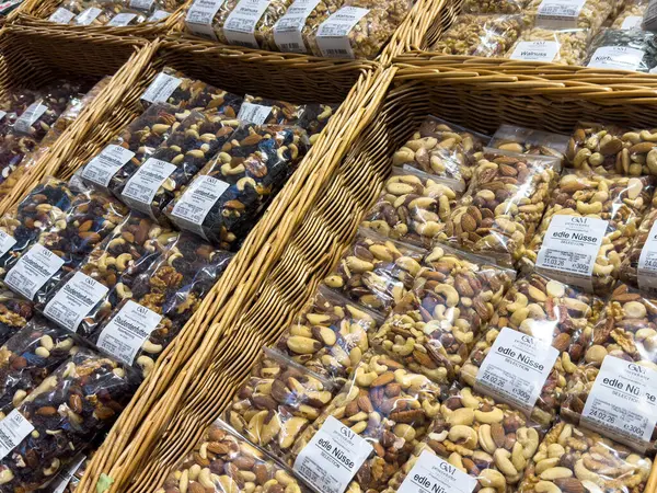 Villach, Avusturya - 21 Ağustos 2025: Şeffaf poşetlerdeki çeşitli fındıklar, canlı renkler ve dokuların ön plana çıkarıldığı bir pazarda örülmüş sepetler halinde düzenleniyor