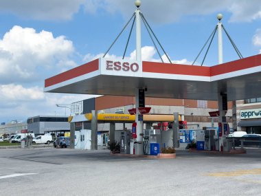 Udine, İtalya - 26 Ağustos 2025: Esso benzin istasyonunda, açık gökyüzü ve yakınlardaki binaların bulunduğu ticari bir alanda modern tasarım ve canlı tabela yer alıyor.