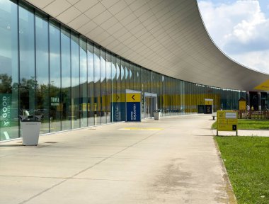 Udine, İtalya - 26 Ağustos 2025: Çağdaş cam yapı, süpürücü bir çatı, renkli tabela ve yeşil peyzaj içeriyor ve ziyaretçiler için davetkar bir ortam yaratıyor