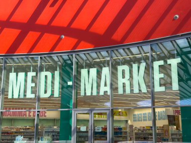 Udine, İtalya - 26 Ağustos 2025: MEDI-MARKET mağaza vitrininde eczane ürünlerini gösteren büyük cam pencereler, canlı kırmızı çatı davetkar alışveriş deneyimine ekleniyor