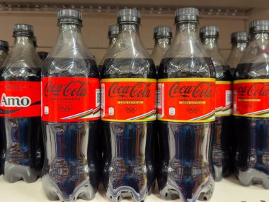 Udine, İtalya - 26 Ağustos 2025: Coca-Cola şişeleri, simgesel markalaşma ve renkli Olimpiyat tasarım elementlerinin yer aldığı bir rafta düzgünce düzenlendi