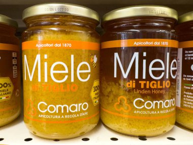 Udine, İtalya - 26 Ağustos 2025: Ihlamur balı içeren Miele di Tiglio 'nun Comaro kavanozları renkli etiketli bir süpermarket rafında cazip bir şekilde düzenlenmiştir.